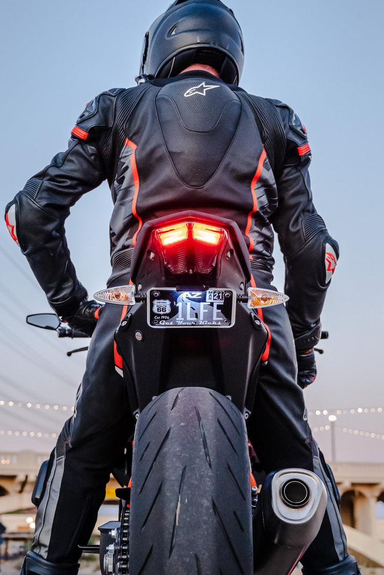 Motorcyclist in leathers on a sportbike at dusk with its LED tail light and turn signals lit